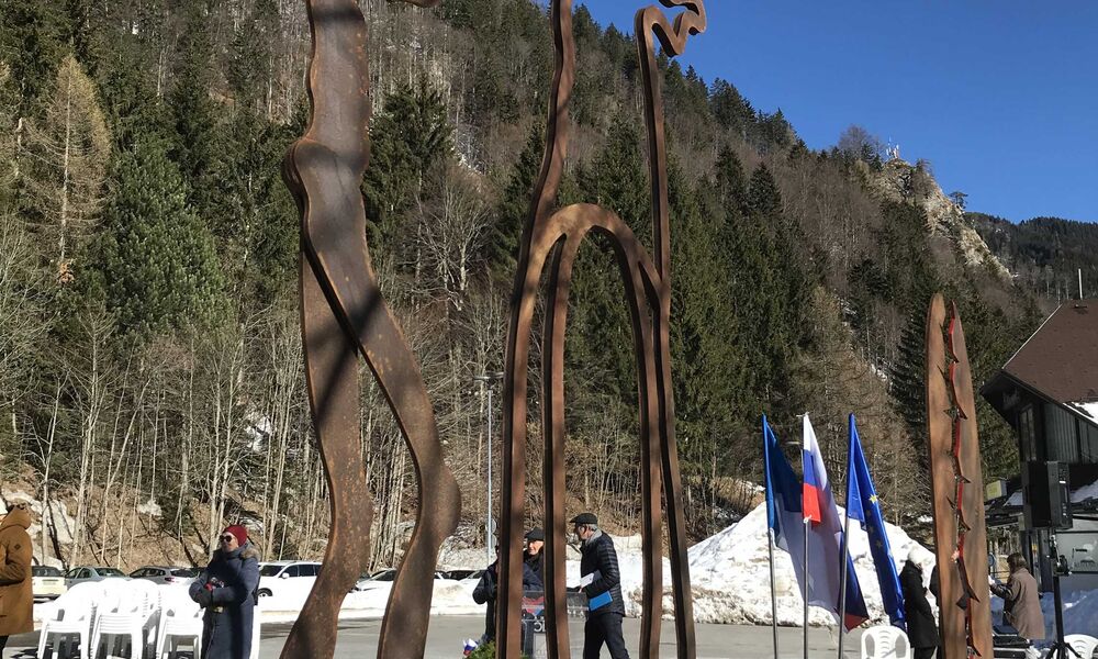 Eine rostfarbene Skulptur auf einem Parkplatz, im Hintergrund Wald