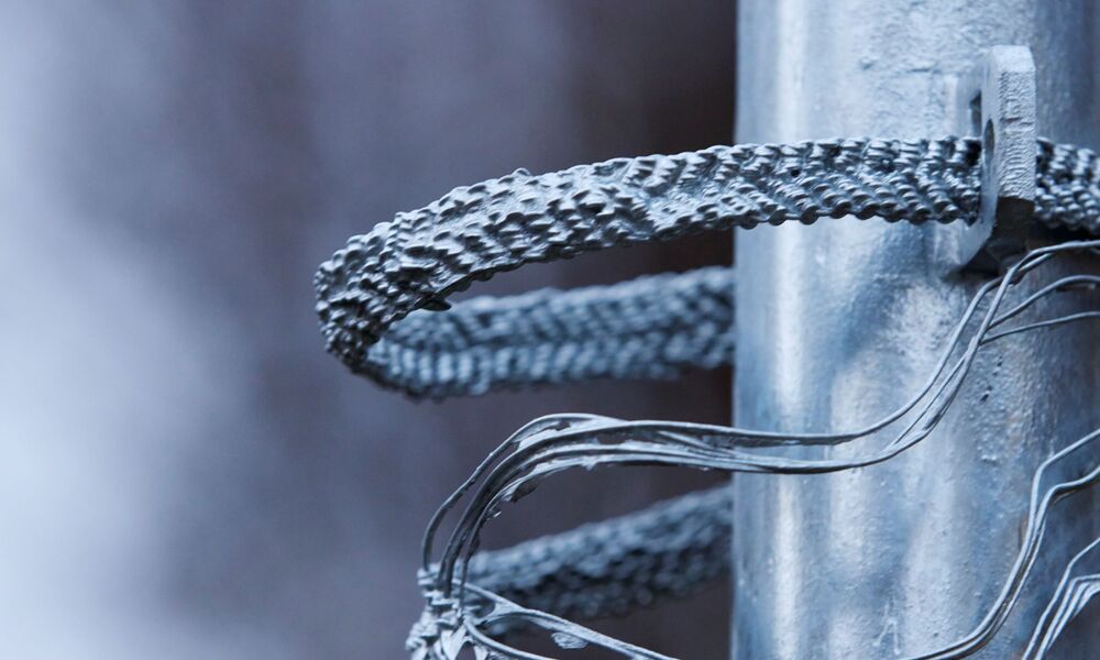 Auf der Nahaufnahme eine Metallstange zu sehen, um die sich mehrere verdrillte, silbrig glänzende Drahtstücke winden.