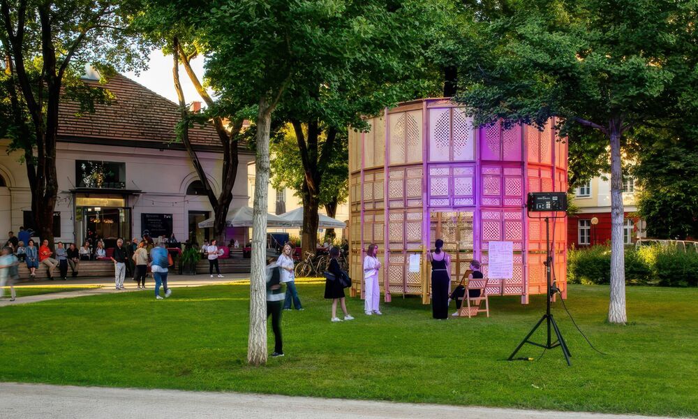 In einem Park ist ein runder breiter Turm errichtet, mehrere Personen stehen und sitzen darum
