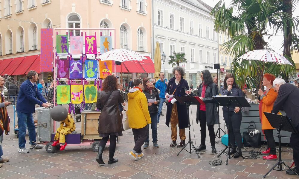 Mehrere Frauen stehen mit Mikrofon und Kunstwerken am Alten Platz in Klagenfurt