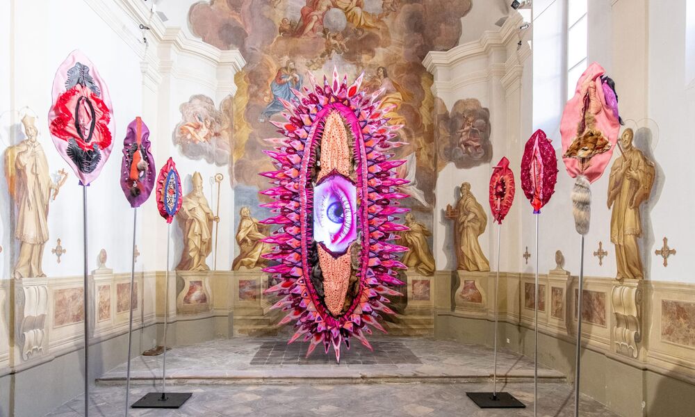 Ein überdimensionales rosafarbenes Objekt mit einem Auge in der Mitte steht in einer kleinen Kapelle