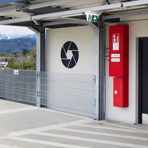 Das Foto zeigt ein Kunstwerk aus farbigen horizontalen Steifen und ein kreisförmiges Objekt an der Wand eines Gebäudes.