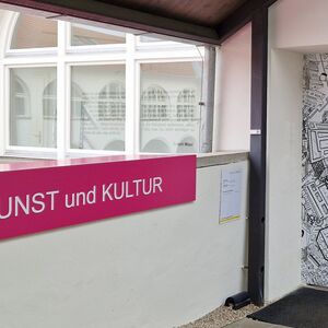 Heller Eingangsbereich mit weißer Brüstung und pinkfarbenem Schriftzug - Kunst und Kultur