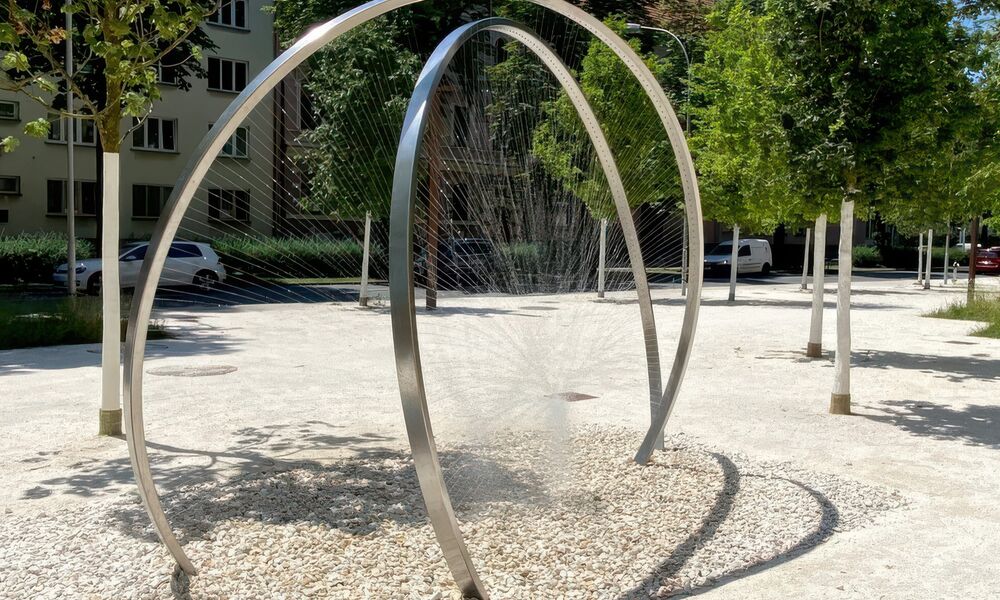 Zwei metallene Bögen, aus denen Wasserstrahlen in die Mitte schießen