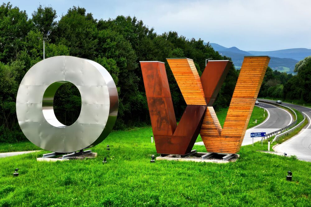 Die Buchstaben O und W als große Skulpturen aus Metall und Holz auf einer grünen Wiese neben einer Autobahnauffahrt