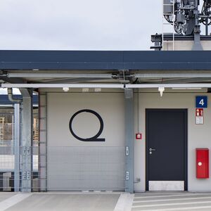Farbige horizontale Streifen und ein rundes Objekt mit einem Strich an der Unterseite an der Außenwand eines Gebäudes auf einem Parkdeck.