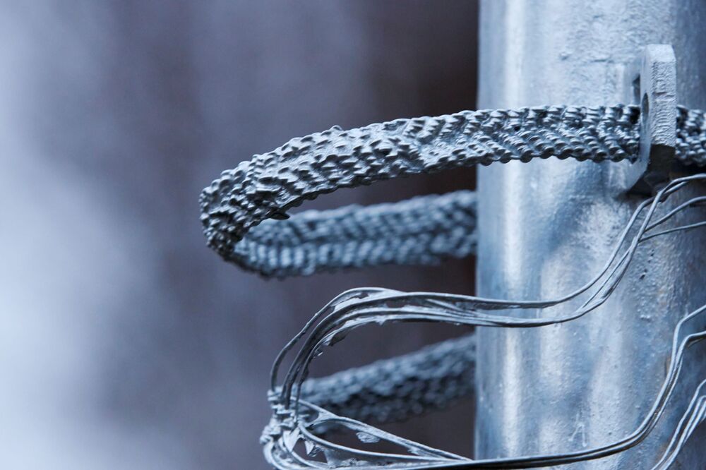 Auf der Nahaufnahme eine Metallstange zu sehen, um die sich mehrere verdrillte, silbrig glänzende Drahtstücke winden.