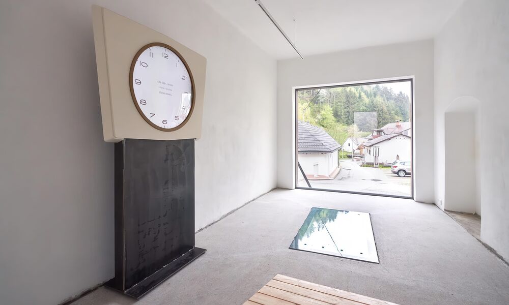 Ein heller leerer Raum, darin eine überdimensionale Uhr ohne Zeiger