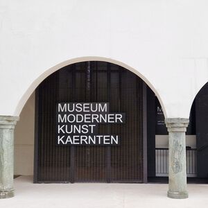 Schwarzer Stiegenaufgang unter hellen Arkaden mit dem Schriftzug Museum Moderner Kunst Kärnten