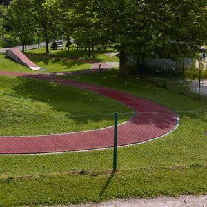 Grüne Wieser die durch einen Zaun begrenzt wird. Ein roter kreisförmiger Weg begrenzt die Wiese.